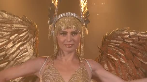 Underbar kvinnlig skådespelerska klädd som den grekiska gudinnan Artemis med vingar. En smal kvinna i guldkostym och huvudbonad dansar mot bakgrund av studioljus. Närbild. — Stockvideo
