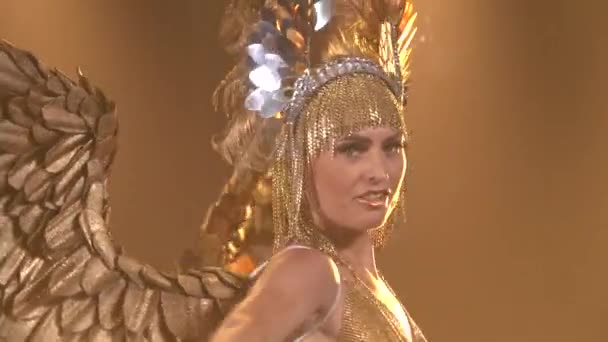 Nádherná herečka oblečená jako řecká bohyně Artemis s křídly. Štíhlá žena ve zlatém obleku a s čelenkou tančí na pozadí studiového světla. Zavřít. — Stock video