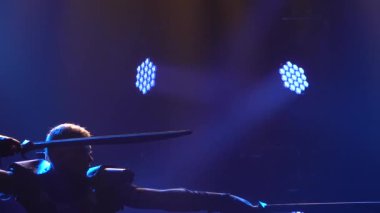 Zırhlı bir şövalyenin silueti iki kılıcı profesyonel olarak kullandığını gösterir. Duman ve mavi ışıklı karanlık stüdyo. Ağır çekim. Kapat..