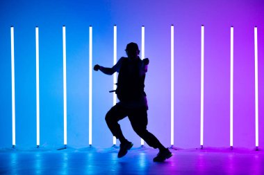 Genç break dansçı, neon lambalarla renkli arka planda hip-hop dansı yapıyor. Breakdance dersleri. Kapat..