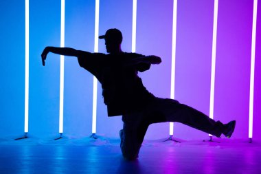 Genç yakışıklı adam şık kıyafetlerle break dans yapıyor. Neon ışıklı arka plan. Akrobatik bboy dansçısı. Breakdance okulu posteri. Kapat..
