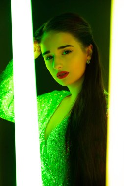 Parlak makyajlı, karanlık bir stüdyoda neon tüplerin arkasında poz veren muhteşem genç bir kadın model. Portreyi kapat.