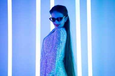 Güneş gözlüklü güzel bir kadının parlak, modaya uygun stüdyo portresi neon tüplerin arka planına karşı. Seksi tarz, sevimli duygular. Kapat..