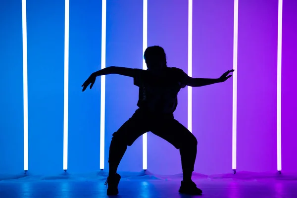 Jeune femme dansant street dance hip hop dans un studio avec tube lumineux néon sur fond bleu violet. Silhouette sombre. Design d'affiches de danse et de musique. — Photo