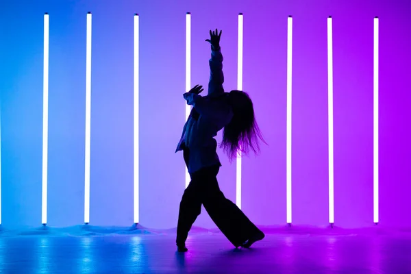 Attraktiv ung kvinna dansare dansar samtida i studion på en blå lila bakgrund med neon belysning lampa. — Stockfoto
