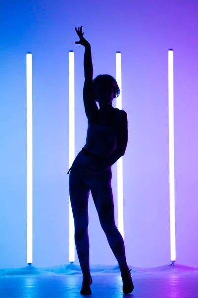Elegante mujer joven bailando elementos de la danza moderna en el estudio sobre un fondo azul púrpura con lámpara de iluminación de neón. Diseño de cartel de danza. — Foto de Stock