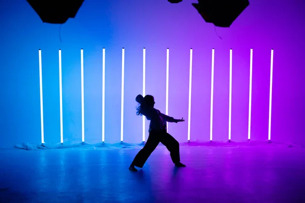 Attraktiv ung kvinna dansare dansar samtida i studion på en blå lila bakgrund med neon belysning lampa. — Stockfoto