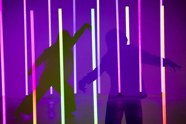 Коллаж теней изящная молодая женщина танцует элементы современного танца в студии на синем фиолетовом фоне с неоновой лампой освещения. Дизайн танцевальных плакатов. — стоковое фото