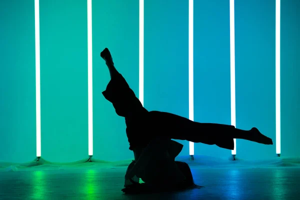 年轻女街头舞者的轮廓在一个有霓虹灯照明管的工作室里跳舞，做体操练习。舞蹈和音乐海报设计. — 图库照片