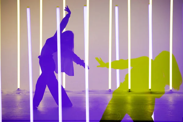 Colagem de sombras moderno jovem dançando single no estúdio em um fundo colorido com tubo de iluminação de néon. — Fotografia de Stock