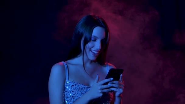 Portræt af charmerende ung kvinde sms 'er på sin telefon og smiler flirtende. Tæt på. Langsom bevægelse. – Stock-video