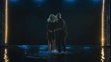 Dans eden güzel çift Latin dansı. Siyah elbiseli profesyonel dansçılar suyun yüzeyinde salsa yapıyor. Arka plandaki karanlık stüdyo. Yavaş çekim.