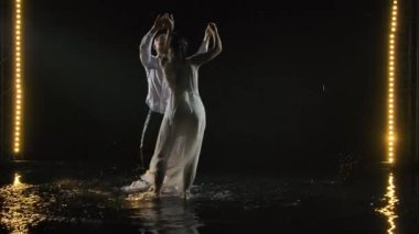 Beyaz elbiseli bir erkek ve kadın tutkuyla salsa yapıp dans ediyorlar. Çift suyun yüzeyinde dans eder ve birçok sıçrama yaratır. Yavaş çekim.