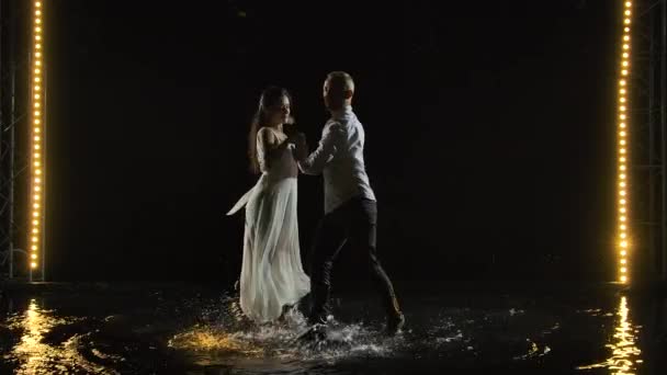 Una pareja bailando salsa en blanco. Baile hermoso caliente apasionado realizado en un estudio oscuro en una superficie de agua con muchas salpicaduras. Movimiento lento. — Vídeo de stock