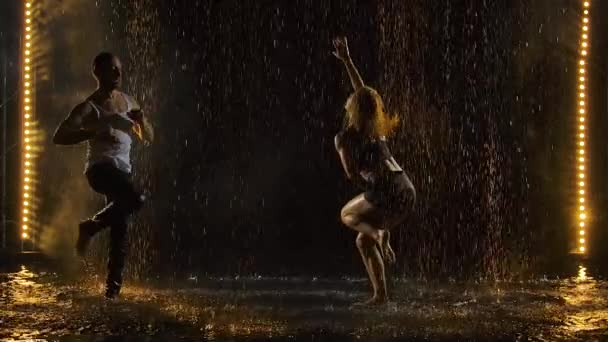 Bailarines hábiles bailan salsa en una habitación oscura bajo las luces del concierto y el humo. La sensual pareja realiza una danza artística y emocional entre las gotas de lluvia y muchas salpicaduras. Movimiento lento. — Vídeo de stock