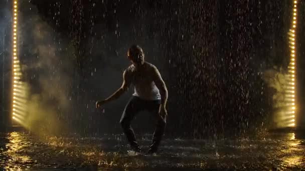 Silueta de un bailarín bailando elementos de salsa en la superficie del agua entre gotas de lluvia y salpicaduras de agua. Movimiento lento. — Vídeos de Stock