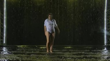 Islak esmer, yağmurda dans etmenin elementlerini güzel stüdyo ışıklarının ve dumanın arka planına karşı gösteriyor. Tutkulu Latin Amerika dansı ağır çekimde.