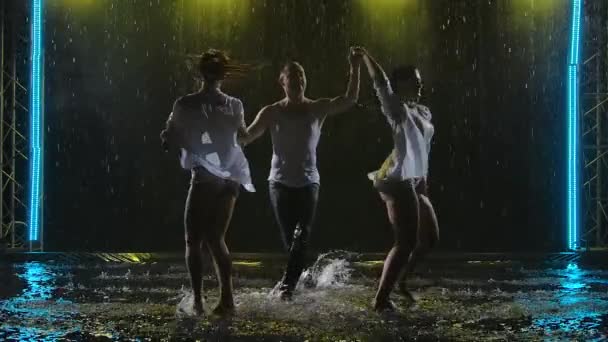 Bailarines profesionales Silhouette bailando un apasionado baile de salsa en gotas de lluvia sobre un fondo oscuro estudio. Dos mujeres y un hombre practican latino en un estudio ahumado en la superficie del agua. Movimiento lento — Vídeos de Stock