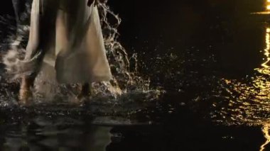 Profesyonel dansçılar karanlık bir stüdyoda su yüzeyinde çıplak ayakla dans ediyorlar. Bacaklar dansta birçok sıçrama yaratır. Ağır çekimde yakın çekim.