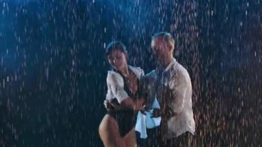 Parlak yağmur damlaları ve stüdyo ışıkları arasında dans eden çiftlerin tutkulu hareketleri. Bedenleri yakınlaştıran bir dans. Ağır çekim. Kapat..