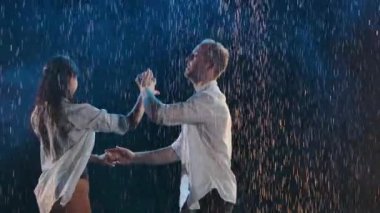 Parlak yağmur damlaları ve stüdyo ışıkları arasında dans eden çiftlerin tutkulu hareketleri. Bedenleri yakınlaştıran bir dans. Ağır çekim. Kapat..