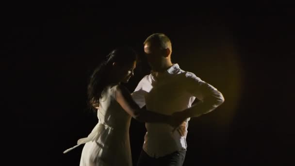 Linda pareja sonriente bailando salsa en un estudio oscuro. Un hombre y una mujer con ropa blanca están disfrutando del baile. En cámara lenta. De cerca.. — Vídeos de Stock