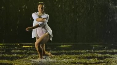 Yağan yağmurda dans eden kadın dansçı. Islak elbiseli, danstan zevk alan bir kadının silüeti. Ağır çekim. Kapat..