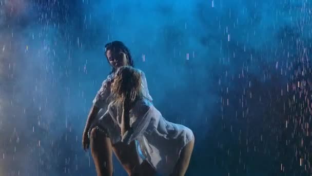 Çekici, tutkulu sarışın ve esmer dansçıları. Parlak yağmur ve dumanın arka planında birbirlerini okşarlar. Islak kadınlar erotik olarak ağır çekimde hareket ederler. Kapat.. — Stok video