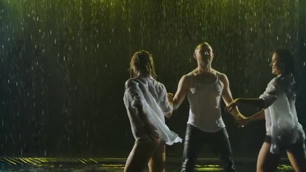짙은 연기가 자욱 한 배경에서 비가 내리는 가운데 살사 춤을 추는 행렬. 세 사람의 젖은 몸으로 된 실루엣 하나가 서서히 유혹적으로 움직 인다. 닫아. — 비디오