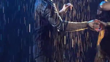 Islak bir adam ve siyah elbiseli bir kadın tutkulu bir şekilde salsa dansı yapıyorlar, yağmur damlaları arasında dönüp duruyorlar. Bir çift karanlık bir stüdyoda sahne ışıklarıyla dans ediyor. Ağır çekimde kapat..