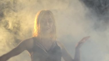 Karanlık bir stüdyoda yağmurda salsa yapan sevimli, gülümseyen sarışın kadın. Yağmurdan ıslanan dansçı dansın tadını çıkarıyor. Ağır çekim. Kapat..