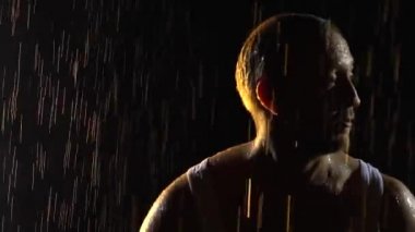 Karanlık dumanlı bir stüdyoda, yağmurun altında dans eden erkek dansçılar. Islak beyaz atletli bir adamın silüeti dansı seviyor. Gövde ağır çekimde yaklaşsın..