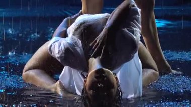 Çekici, tutkulu sarışın ve esmer dansçı yağmurda birbirlerini okşarlar. Islak kadınlar erotik olarak karanlık dumanlı bir stüdyonun arka planında ağır çekimde hareket ederler. Kapat..