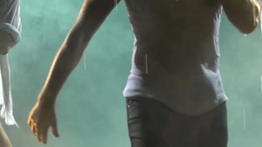 Karanlık dumanlı arka planda salsa dansının tutkulu hareketleri. Yavaş çekimde baştan çıkarıcı hareket eden üç ıslak vücuttan oluşan bir siluet. Bir erkek ve bir kadının gövdesi birbirine yakın..