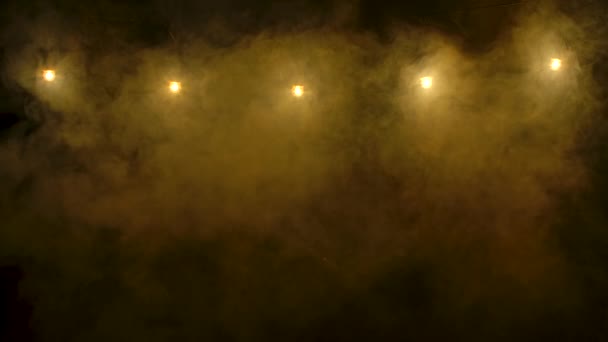 Uma nuvem de fumaça iluminada pela luz de néon amarelo se levanta contra o fundo das lâmpadas em chamas. Filmado num estúdio escuro. Fecha. Movimento lento. — Vídeo de Stock