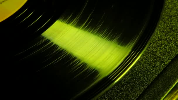 Imágenes macro de un disco de vinilo giratorio en cámara lenta golpeando un haz de luz de neón amarillo. Antiguo gramófono retro tocando música. Vista superior. De cerca.. — Vídeo de stock