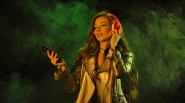 Genç ve güzel bir kadının portresi büyük kırmızı kulaklıklarla akıllı telefondan dans edip müzik dinlemektir. Kapatın. Yavaş çekim.