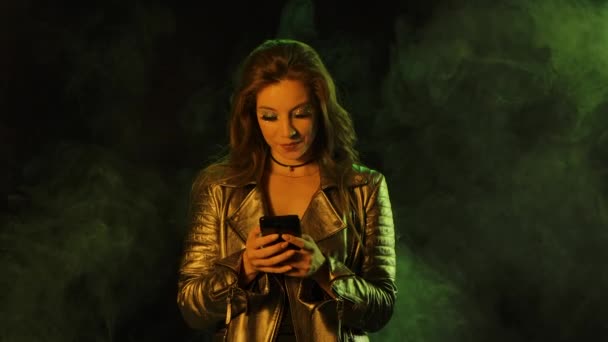 Retrato de una joven mujer bonita está enviando mensajes de texto en su teléfono y luego muestra el teléfono inteligente con una tecla de croma de pantalla azul y muestra el gesto de pulgares hacia arriba. De cerca. Movimiento lento. — Vídeo de stock