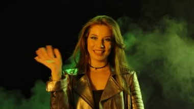 Genç ve güzel bir kadının portresi kameraya bakıyor. Birini görmüş, el sallıyor ve buraya el hareketi yapıyor. Kapatın. Yavaş çekim.