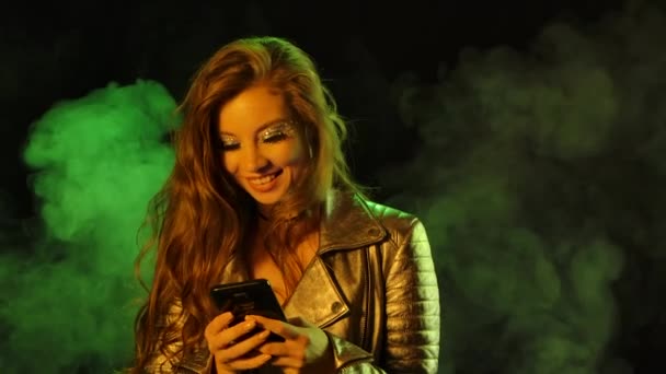 Retrato de mujer bonita joven está enviando mensajes de texto con alegría en su teléfono y luego muestra el teléfono inteligente con una tecla de croma de pantalla azul. De cerca. Movimiento lento. — Vídeos de Stock