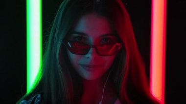 Şık güneş gözlüklü güzel bir kadının portresi beyaz kulaklıklı akıllı telefondan dans edip müzik dinlemektir. Kapatın. Yavaş çekim.