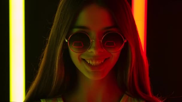 Portrét krásné mladé krásné ženy ve stylových kulatých slunečních brýlích, dívající se do kamery s nadšeným výrazem. Zavřít. Zpomalený pohyb. — Stock video