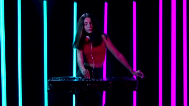 Retrato de una joven mujer bonita con grandes auriculares rojos baila y mezcla música en el tocadiscos DJ. Movimiento lento. — Vídeos de Stock