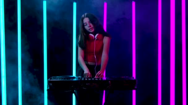 Retrato de una joven mujer bonita con grandes auriculares rojos baila y mezcla música en el tocadiscos DJ. Movimiento lento. — Vídeo de stock