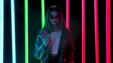 Şık güneş gözlüklü güzel bir kadının portresi beyaz kulaklıklı akıllı telefondan dans edip müzik dinlemektir. Yavaş çekim.