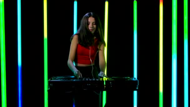 Portrait d'une jeune jolie femme dans un grand casque rouge jouant un ensemble musical tout en dansant près de la platine DJ. Mouvement lent. — Video