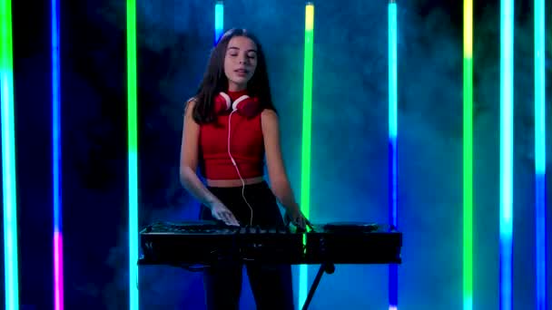 Portret młodej ładnej kobiety w czerwonych słuchawkach tańczącej i grającej na muzycznej konsoli dźwiękowej do miksowania muzyki. Zwolniony ruch. — Wideo stockowe