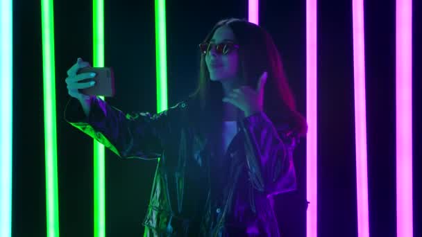 Retrato de una hermosa mujer muy joven en gafas de sol con estilo toma selfies y mensajes de texto en su teléfono. Movimiento lento. — Vídeos de Stock