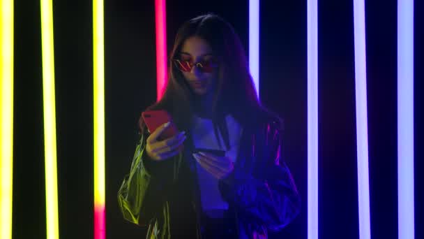 Retrato de una hermosa mujer muy joven en gafas de sol con estilo hace una compra en línea con un teléfono inteligente y una tarjeta de crédito. De cerca. Movimiento lento. — Vídeos de Stock