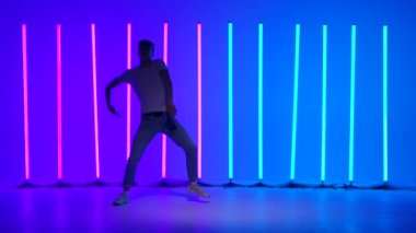 Dans eden ve çağdaş koreografi yapan şık bir gencin silueti. Parlak ışıklı neon ışıkların arasında sokak dansı. Hip hop tekniği öğretme konsepti. Yavaş çekim.